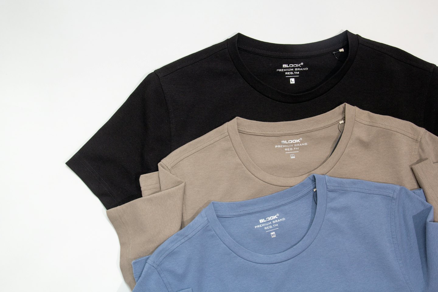 Tres camisetas dobladas en negro, topo y azul claro.