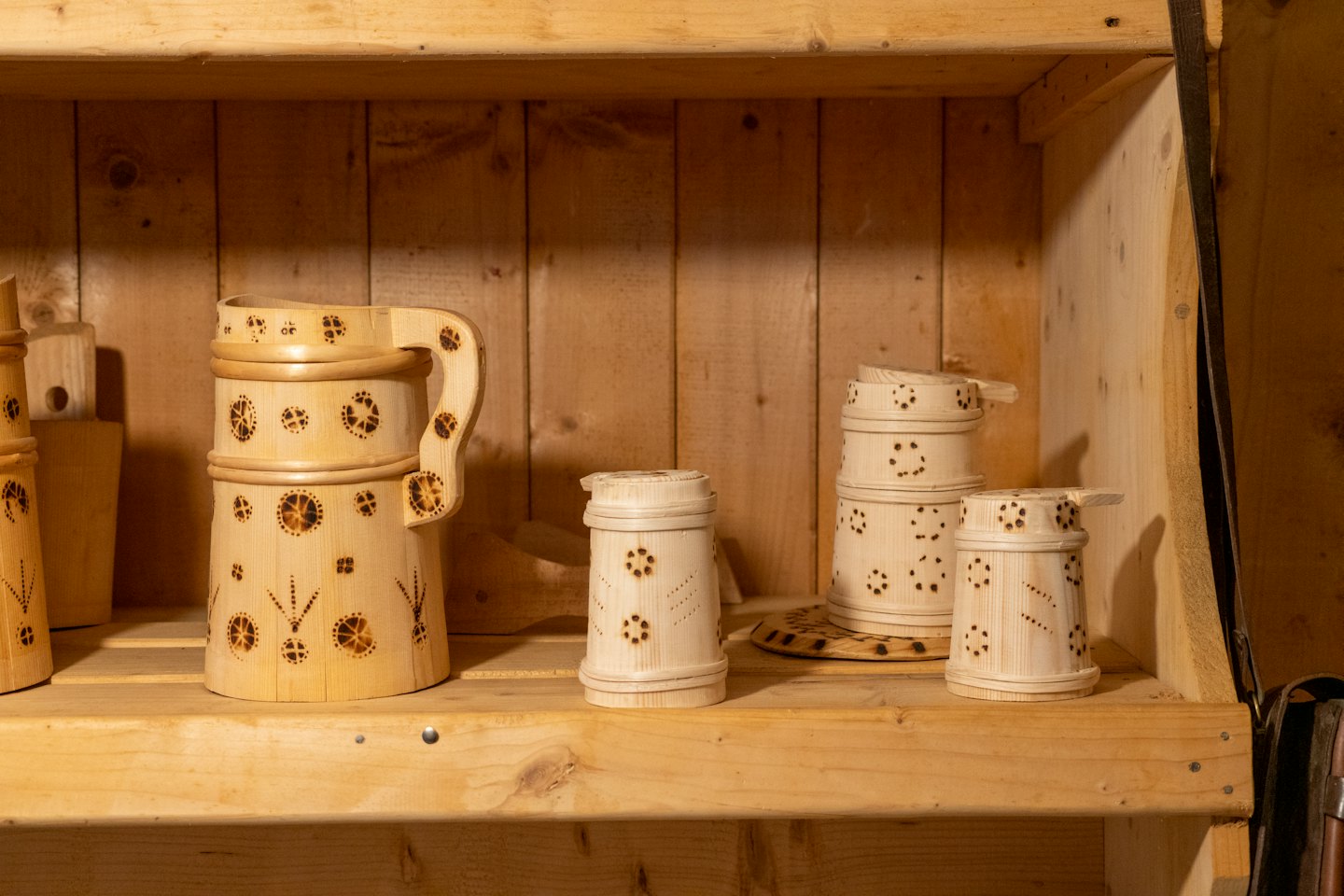 Tazas de madera artesanales con diseños decorativos sobre estantes de madera.