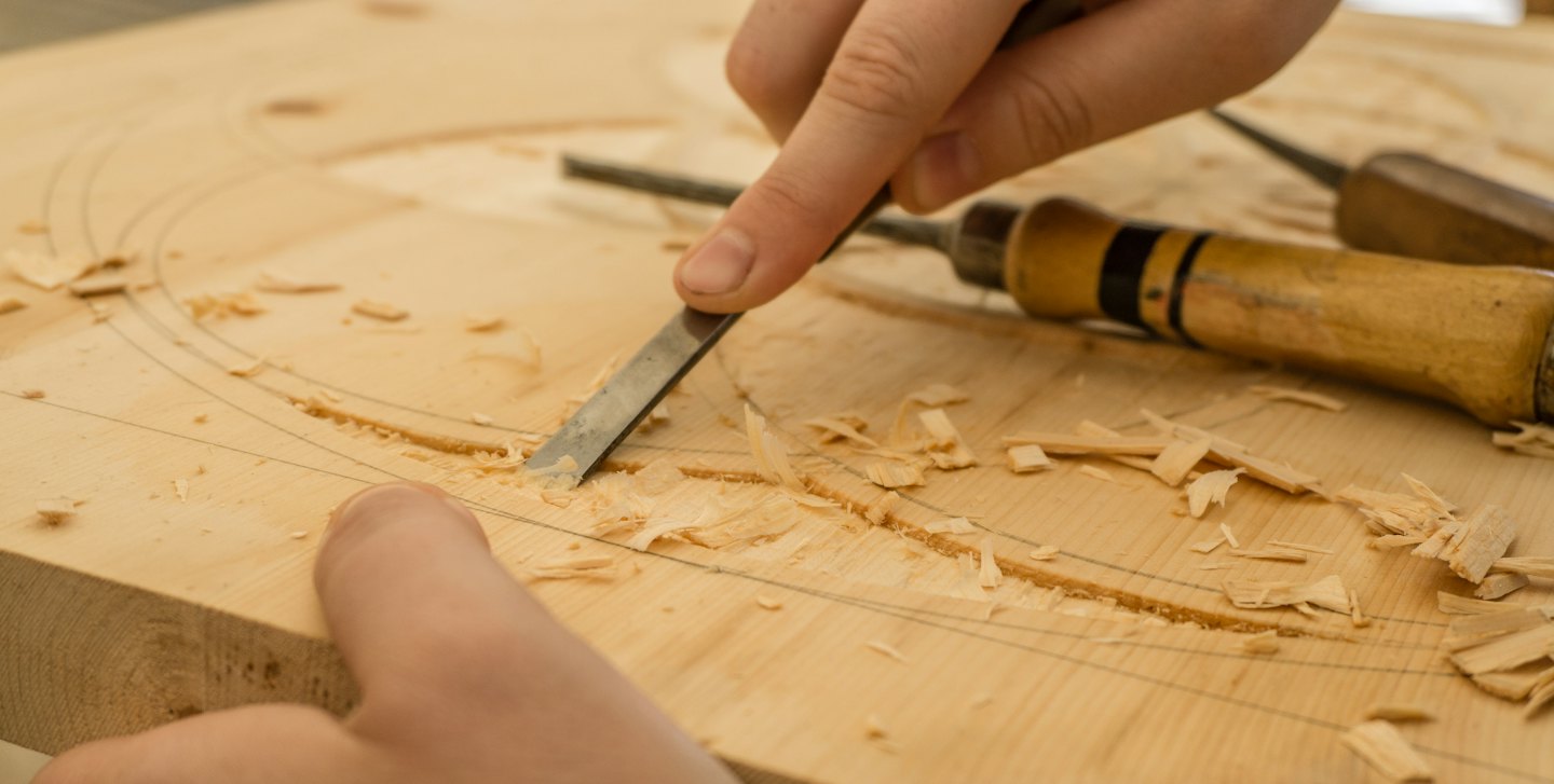 Manos usando un formón para tallar madera.